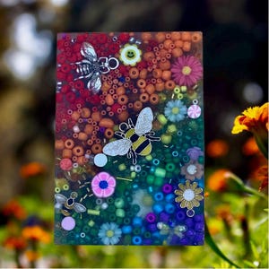 May include: A rectangular resin art piece with a colorful gradient of red, orange, green, and blue. The piece is filled with beads and small flower and bee charms. The bees are silver and yellow.