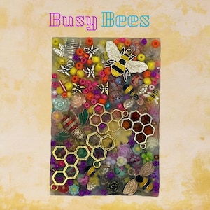 May include: A rectangular artwork with the text "Busy Bees" at the top. The artwork is filled with colorful beads, flowers, and bee-themed embellishments, including gold honeycomb shapes and bee charms. The background is a textured yellow.