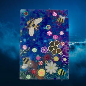 May include: A rectangular resin art piece with a blue background, featuring bees, flowers, and colorful embellishments. The design includes a large bee, a honeycomb, and various decorative elements. The piece is a vibrant and whimsical decorative item.