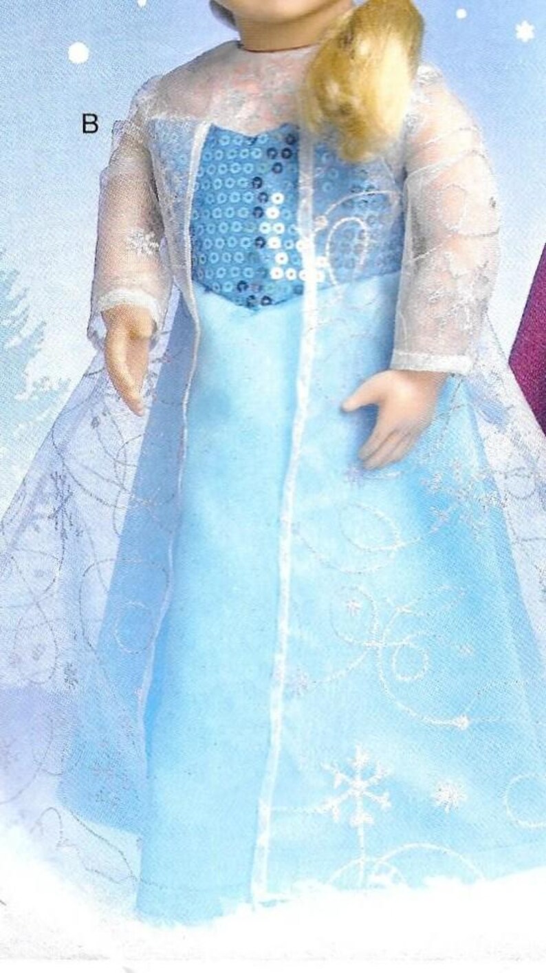 Peut inclure: Poup&eacute;e v&ecirc;tue d'une robe bleu clair avec un corsage &agrave; paillettes et une superposition transparente &agrave; motifs de flocons de neige. La poup&eacute;e a les cheveux blonds et porte une veste transparente &agrave; manches longues. La robe a une longue jupe fluide.