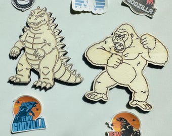 May include: A collection of stickers and wooden cutouts featuring Godzilla and King Kong. Included are two large light-colored wooden figures, a small black and white gorilla with a crown, a blue Bigfoot silhouette, and four colorful decals with text.