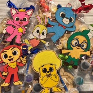 May include: A set of six wooden paint-your-own character figures, including a pink fox, a blue bear, a yellow mushroom, a green creature with glasses, a yellow bunny, and a red monkey. The figures are packaged in clear plastic bags with paint pots and paintbrushes.