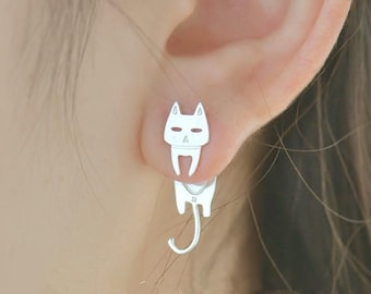 Könnte beinhalten: Silberne Ohrringe mit Katze. Die Katze schaut nach vorne, der Schwanz hängt nach unten. Die Ohrringe sind minimalistisch gestaltet.