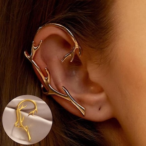May include: A gold-colored ear cuff featuring a branch-like design. The ear cuff wraps around the ear, with the branch extending along the outer ear and curving around the top. A smaller version of the ear cuff is shown in a circular inset.