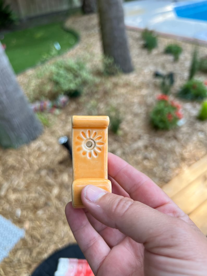 Peut inclure: Un crochet en c&eacute;ramique avec un motif floral de couleur orange clair. Le crochet a un petit trou au centre du motif.