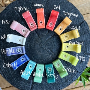 Peut inclure: Un ensemble de 15 crochets en c&eacute;ramique de diff&eacute;rentes couleurs, notamment mangue, rouge, framboise, mandarine, or, souci, citron vert, vert, aqua, aruba, cactus, blanc, violet, cobalt et rose. Chaque crochet est orn&eacute; d'un petit motif floral.
