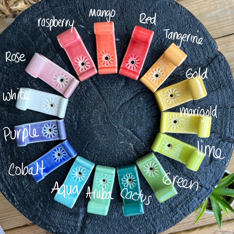 Peut inclure: Un ensemble de 15 crochets en c&eacute;ramique de diff&eacute;rentes couleurs, notamment mangue, rouge, framboise, mandarine, or, souci, citron vert, vert, aqua, aruba, cactus, blanc, violet, cobalt et rose. Chaque crochet est orn&eacute; d'un petit motif floral.