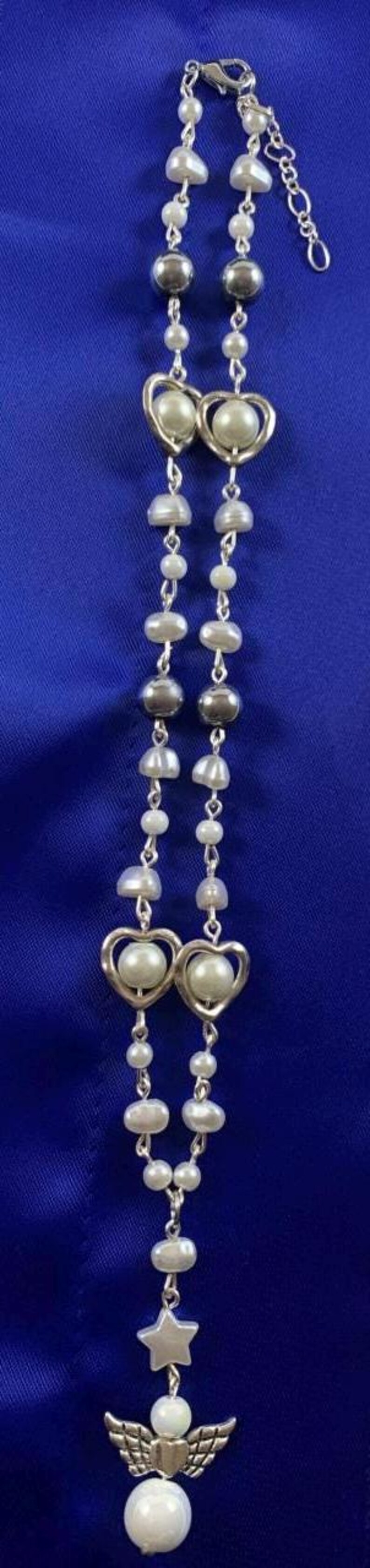 Puede incluir: Un collar de cadena de plata con cuentas de perlas blancas y dijes de coraz&oacute;n de plata. El collar tiene un dije de &aacute;ngel de plata con una estrella y una cuenta de perla en la parte inferior.