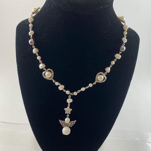 Puede incluir: Un collar de plata con perlas blancas y dijes de coraz&oacute;n y estrella plateados. El collar tiene un dije de &aacute;ngel colgante con una perla en el centro.