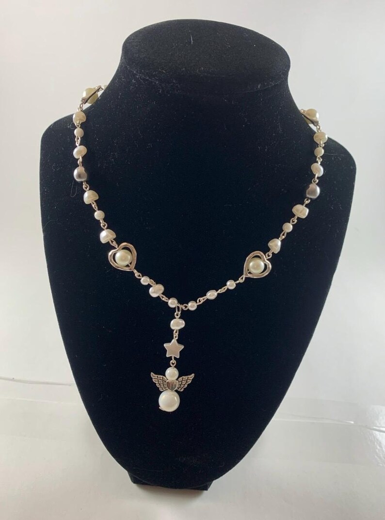 Puede incluir: Un collar de plata con perlas blancas y dijes de coraz&oacute;n y estrella plateados. El collar tiene un dije de &aacute;ngel colgante con una perla en el centro.