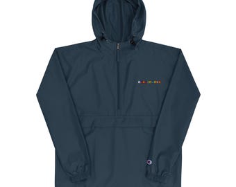 May include: A navy blue hooded anorak jacket with a half-zip closure and a small embroidered design in multiple colors. The jacket features a Champion logo on the lower right side.