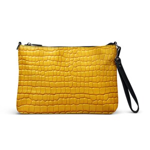 May include: A yellow clutch purse with a black strap and a crocodile-embossed texture.