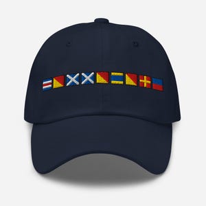 May include: A navy blue baseball cap with a row of colorful nautical signal flags embroidered on the front. The flags are red, white, blue, and yellow.