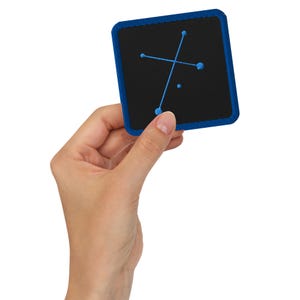 Könnte beinhalten: Ein quadratischer schwarzer Aufnäher mit blauem Rand und blauem Stickdesign. Das Design zeigt eine kreuzartige Form mit drei Punkten und einem einzelnen Punkt. Der Aufnäher wird in der Hand einer Person gehalten.