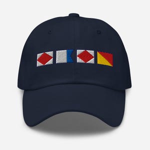 May include: A navy blue baseball cap featuring embroidered nautical signal flags in red, white, blue, and yellow. The cap has a curved peak and a six-panel design, ideal for sun protection.