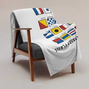 May include: White fleece blanket with a black and white alphabet flag design. The flags are arranged in alphabetical order from Charlie to November.
