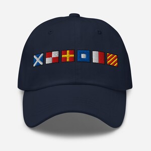 May include: Navy blue baseball cap with embroidered nautical signal flags in white, red, yellow, and blue. The cap features a curved brim and a six-panel design, suitable for sun protection and casual wear.