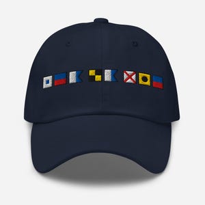 May include: A navy blue baseball cap with a row of colorful nautical signal flags embroidered on the front. The flags are red, white, blue, yellow, and black.