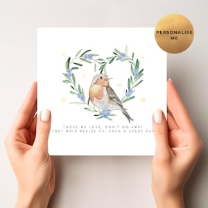 May include: A white card with a watercolour illustration of a robin inside a heart-shaped wreath of foliage and blue flowers. The card includes the text "THOSE WE LOVE, DON'T GO AWAY THEY WALK BESIDE US, EACH & EVERY DAY."