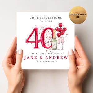 May include: A white card held by hands, with a ruby wedding anniversary design. The card shows the number "40" in red, and text that reads "Congratulations on your Ruby Wedding Anniversary, Jane & Andrew, 19th June 2025". A gold circle says "Personalise Me".