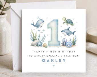 May include: A square greeting card featuring a large light blue number one surrounded by watercolor illustrations of a whale, turtle, shark, starfish, and seashells. The text reads: HAPPY FIRST BIRTHDAY TO A VERY SPECIAL LITTLE BOY OAKLEY.
