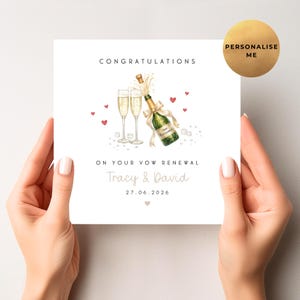 May include: A white card with the text "Congratulations" and "On Your Vow Renewal". It features a watercolour illustration of champagne glasses, a bottle, and hearts. The names "Tracy & David" and the date "27.06.2026" are also printed on the card.