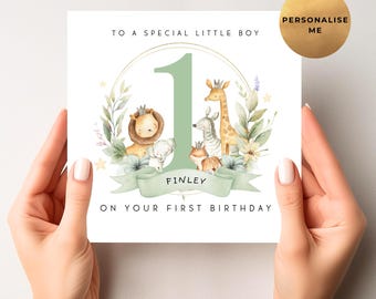Op de afbeelding: Een witte verjaardagskaart met een groen nummer één en de tekst "TO A SPECIAL LITTLE BOY" en "ON YOUR FIRST BIRTHDAY". De kaart bevat illustraties van een leeuw, een olifant, een zebra, een giraffe en een vos. De naam "FINLEY" staat ook op de kaart.
