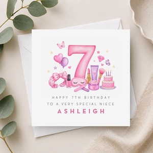 May include: A square greeting card featuring a large pink number 7 surrounded by watercolour illustrations of a headband, nail polish, lipstick, makeup brush, cream jar, cake, balloons, and butterflies. Text reads: HAPPY 7TH BIRTHDAY TO A VERY SPECIAL NIECE ASHLEIGH.