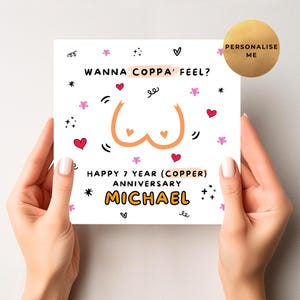 May include: A white greeting card held by hands, featuring the text "WANNA COPPA' FEEL?" and "HAPPY 7 YEAR (COPPER) ANNIVERSARY MICHAEL". The card has a cartoon illustration of breasts and decorative hearts and stars.
