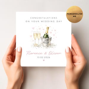 May include: A white wedding card with the text "Congratulations on Your Wedding Day." It features a watercolour illustration of champagne glasses, a bottle in an ice bucket, and the names "Florence & Oliver" with a date.