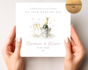 May include: A white wedding card with the text "Congratulations on Your Wedding Day." It features a watercolor illustration of champagne glasses, a bottle in an ice bucket, and the names "Florence & Oliver" with a date.