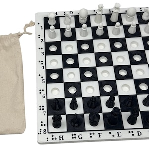 May include: A black and white chess set with braille markings on the side. The board has a checkerboard pattern. The chess pieces are black and white. A beige drawstring bag is to the left of the board.