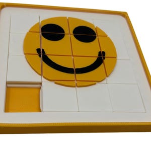 May include: A yellow and white puzzle featuring a smiling face design. The puzzle is composed of several square pieces that fit into a yellow tray. The smiley face is yellow with black eyes and a black curved mouth. One piece is missing from the puzzle.