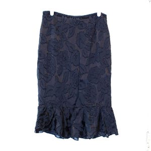 May include: A navy blue skirt with a floral pattern and a ruffled hem. The skirt is hanging on a white hanger against a white background. The floral pattern appears to be embossed or textured.