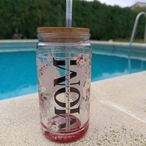 May include: A clear glass tumbler with a bamboo lid and a clear straw. The tumbler features the word "MOM" in large black letters, with "life is the best life" in smaller text. Floral designs in pink and white decorate the glass.