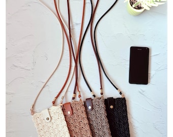 May include: Four crochet phone crossbody bags in cream, tan, brown, and black, each with a matching strap. The bags have a button closure and are displayed with a black smartphone and a small potted plant.