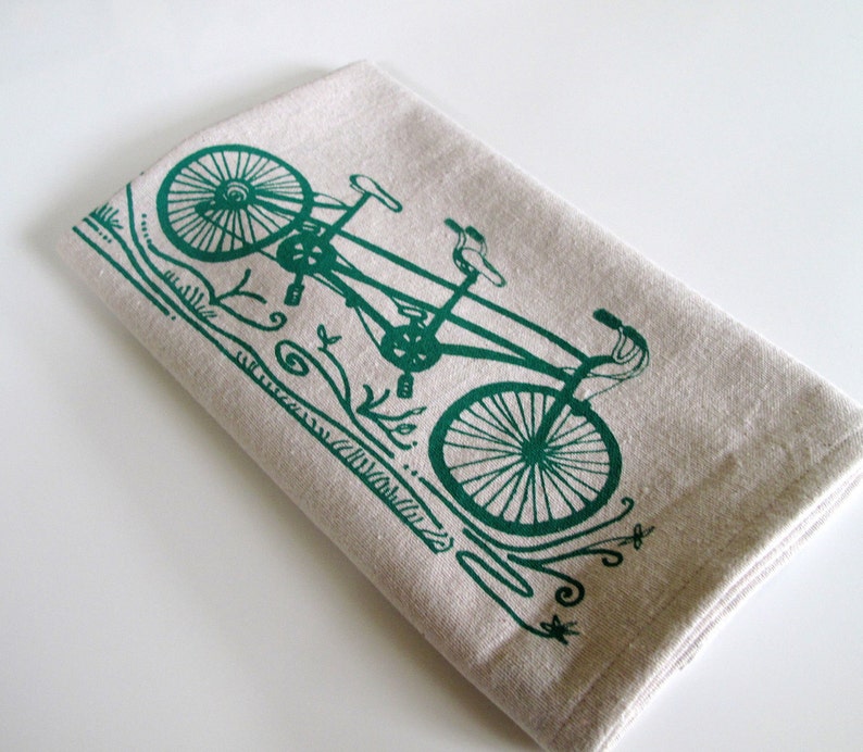 May include: A green tandem bicycle printed on a beige linen tea towel. The bicycle has two seats and handlebars.