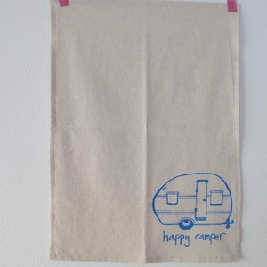 Puede incluir: Una toalla de cocina beige con una ilustraci&oacute;n azul de una caravana y el texto "happy camper".