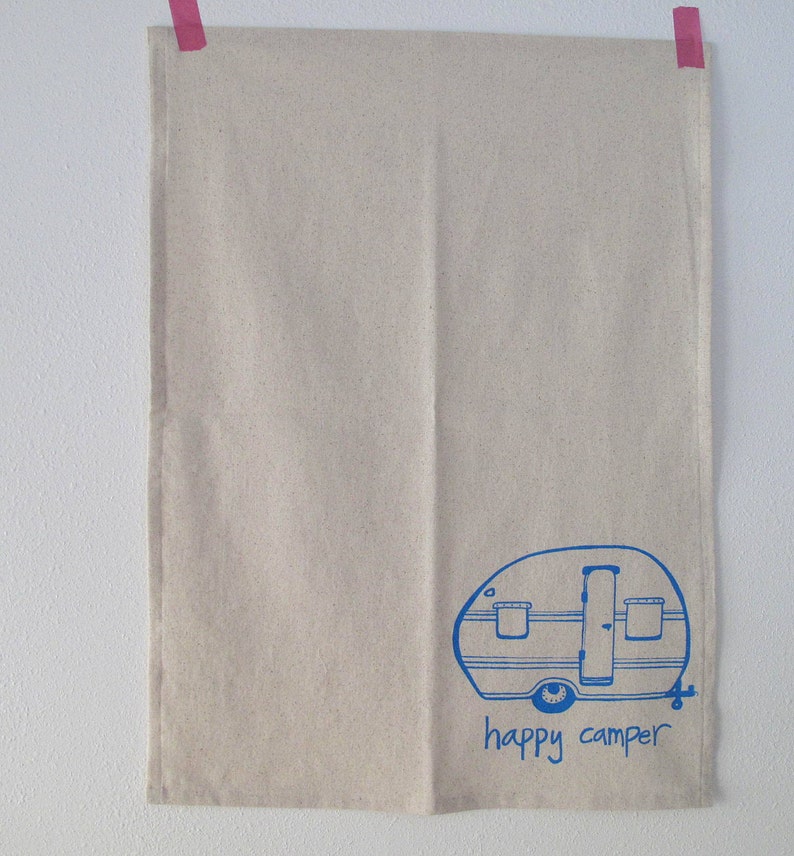 Puede incluir: Una toalla de cocina beige con una ilustraci&oacute;n azul de una caravana y el texto "happy camper".