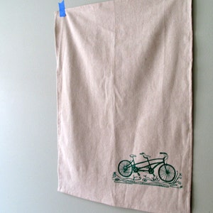 May include: A tan linen tea towel with a green silhouette of a tandem bicycle printed on it.