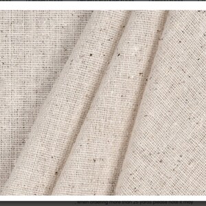 May include: Close-up of a beige fabric with a subtle speckled pattern. The fabric is folded and has a soft, textured appearance.