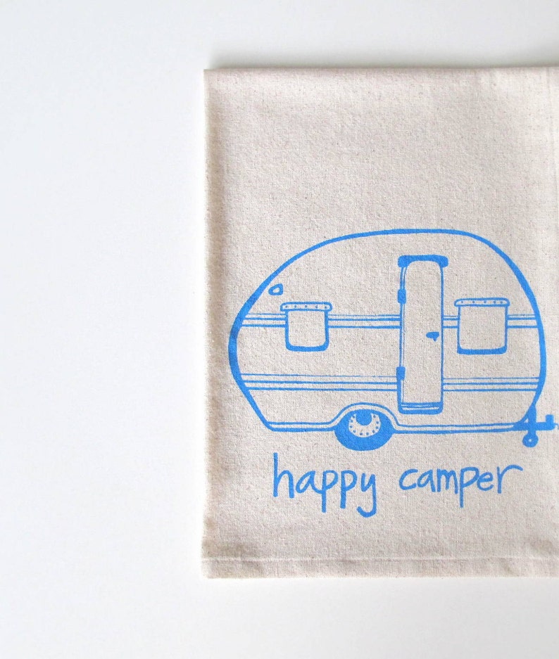 Puede incluir: Una toalla de cocina beige con una ilustraci&oacute;n azul de una caravana y el texto "happy camper".