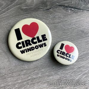 May include: Two round button badges with a white background and black text. The larger badge says "I ♥ CIRCLE WINDOWS PECULIARLY ASHLEY". The smaller badge says "I ♥ CIRCLE WINDOWS". Both badges have a red heart.