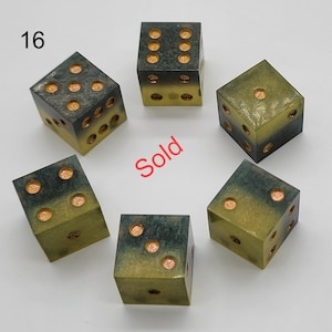 May include: Six dice arranged in a circle, each featuring a gradient from dark charcoal to olive green. The pips are filled with a shimmering copper-colored material. The number 16 is printed in the top left corner, and the word Sold is in red.
