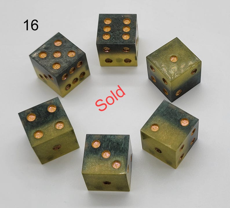 May include: Six dice arranged in a circle, each featuring a gradient from dark charcoal to olive green. The pips are filled with a shimmering copper-colored material. The number 16 is printed in the top left corner, and the word Sold is in red.