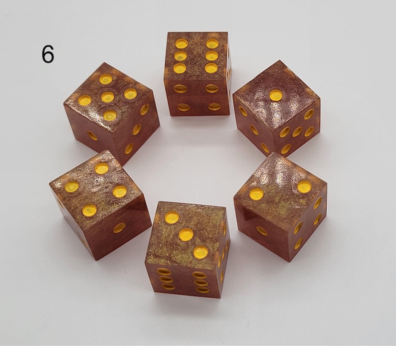 May include: Six square dice arranged in a circle, each featuring a translucent reddish-brown base with embedded gold-colored glitter and bright yellow pips. The number 6 is printed in black in the upper left corner of the image frame.
