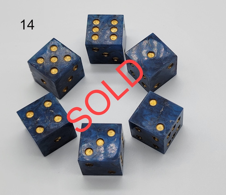 May include: A set of five six-sided dice with a deep blue marbled finish and gold-colored pips. The number 14 is printed in the top left corner, and the word SOLD is overlaid in red across the center of the dice arrangement.