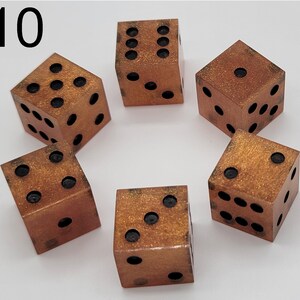 May include: A set of five six-sided dice with a metallic copper finish and gold glitter accents. Each die features black circular pips representing numbers one through six. The number 10 is printed in black in the upper left corner of the image.