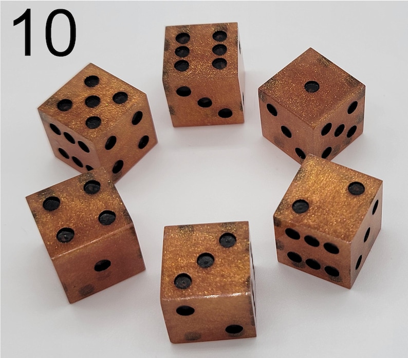 May include: A set of five six-sided dice with a metallic copper finish and gold glitter accents. Each die features black circular pips representing numbers one through six. The number 10 is printed in black in the upper left corner of the image.
