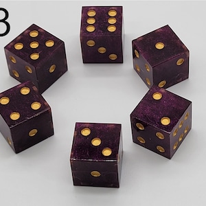 May include: A set of five six-sided dice in a deep purple color with a subtle glittery finish. Each die features recessed circular pips filled with a metallic gold paint. The number 3 is printed in black in the upper left corner of the image.